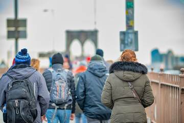 People walking on the promenade of the famous Brooklyn Bridge in winter season, back view. New York...