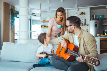 Naklejka premium Father teaching his son how to play guitar. Mom watching. Dad playing some music on a guitar to his son. Playing his favorite song. Father Teaching Son Guitar