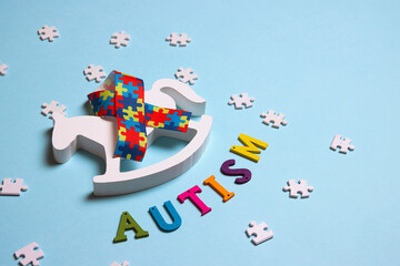 Autism concept with toy rocking horse and and puzzle awareness ribbon on a blue background.