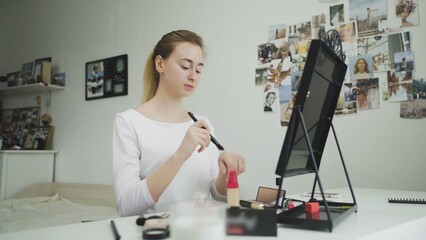 A young woman does her makeup while sitting at a table in front of a mirror