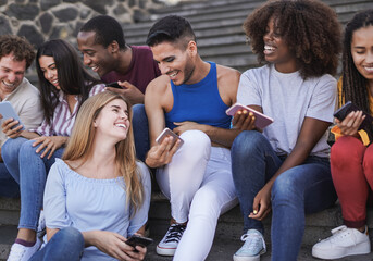 Group of diverse people enjoy day together outdoor - Young multiracial friends using mobile phone in the city