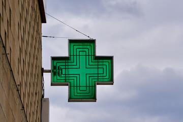 green cross-shaped pharmacy sign with sky in the background