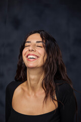 Portrait on dark background of young Turkish girl bursting out laughing with closed eyes