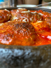 Close-up of meatballs with sauce and melted cheddar cheese in clay pot.