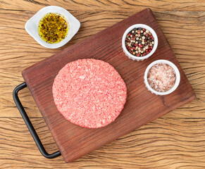 Obraz na płótnie Canvas Raw meat hamburger over wooden board with seasonings
