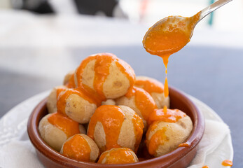 Spoon pouring spicy mojo sauce on papas arrugadas in clay plate. Traditional wrinkled potatoes snack food from Gran Canaria island, Spain. Healthy diet concept - obrazy, fototapety, plakaty