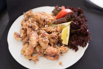 Deep fried baby squids on plate with lemon, lettuce and tomato. Traditional Spanish seafood tapa