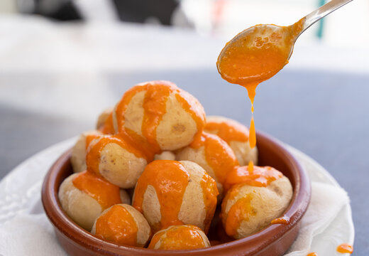 Spoon pouring spicy mojo sauce on papas arrugadas in clay plate. Traditional wrinkled potatoes snack food from Gran Canaria island, Spain. Healthy diet concept