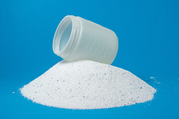 Laundry detergent on a blue background. A measuring cup on a pile of laundry detergent. Household...