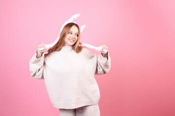 Beautiful girl in rabbit ears on a pink background laugh, Easter holidays. The woman smiles. Looks to the side, space for text, fun.