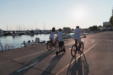 Happy family enjoying a beautiful morning by the sea together, parents riding a bike and their son riding an electric scooter. Selective focus 