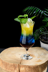 three-color cocktail glass, on a rustic wooden board, vase with plant, black background