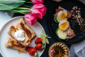 Homemade Easter breakfast top view. Free space for text. Toast with egg, avocado and fish. Russian pancakes with strawberries and sour cream. Holiday breakfast concept.