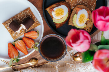 Breakfast with fresh strawberries, a cup of black coffee, fish and avocado sandwiches. Homemade vegetarian breakfast top view. Summer breakfast concept.Glazed cheese in chocolate.