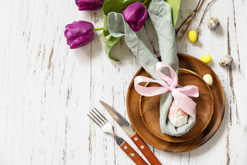 Easter table setting with painted eggs, purple tulip and cutlery on festive table. Table setting for Happy Easter day. Top view flat lay. Copy space.