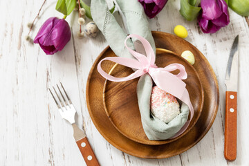 Easter table setting with painted eggs, purple tulip and cutlery on festive table. Table setting for Happy Easter day.
