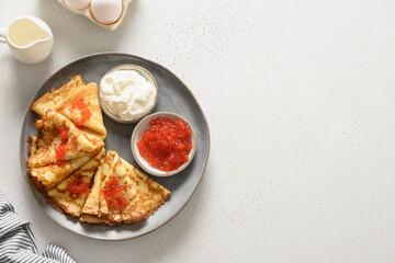 Russian blini with red caviar and sour cream on white background. Top view. Shrovetide. Copy space.