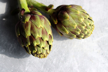 Obraz premium Two fresh artichokes on a table. Close up photo of vegetables on light grey background with copy space. Healthy eating concept. 