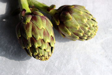 Two fresh artichokes on a table. Close up photo of vegetables on light grey background with copy space. Healthy eating concept.
