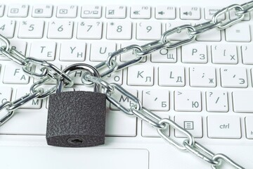 Metal chain and padlock close-up on the background of a white laptop keyboard. Security concept