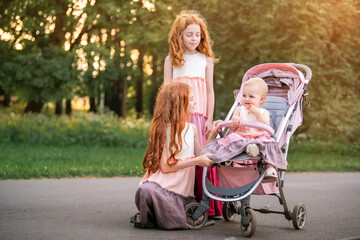 Two older redhead sisters are walking in the park on a sunny summer day with stroller with their...