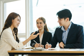 Great business meeting. Three Asian coworkers discussing something with smile while sitting at the office.