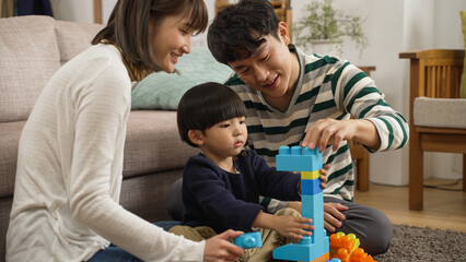 happy japanese family of three enjoying playing plastic building blocks in the living room at home. the father is helping hold the unstable bricks for his son to prevent them fall