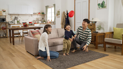 excited asian baby boy playing with a red balloon with his father and mother in the living room at home. they hit the ball trying not to let it fall onto ground © PR Image Factory