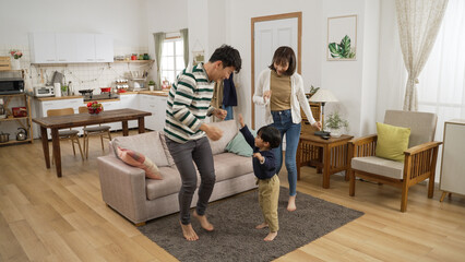 full length shot happy Asian family of three having fun dancing together at home. the baby boy jumping up and down with his father and mother on floor