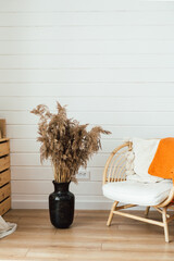 Rattan armchair, floor lamp and large vase with pampas grass in living room interior. Cozy interior in boho style. Real photo