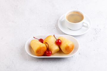 Neapolitan Rum baba on a white plate with a cocktail cherry and a cup of coffee. Small yeast cakes...