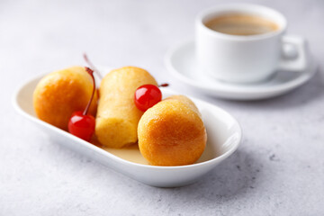 Neapolitan Rum baba on a white plate with a cocktail cherry and a cup of coffee. Small yeast cakes soaked in rum syrup on a gray background. Traditional Italian pastry. Close-up, selective focus.