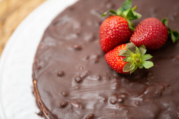 Delicious cake in chocolate glaze with strawberries on a white dish. Puff cake with cream and nuts, decorated with strawberries.