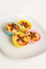 Close-up of homemade vanilla buns with whole almonds in multicolored silicone cups on a white plate. Healthy snack.