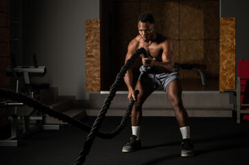 Fototapeta na wymiar Attractive african american man with naked torso doing endurance exercises with trope. 