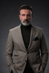 Fototapeta premium Portrait of a stylish elegant senior businessman with a beard and casual business clothes in photo studio isolated on dark background gesturing with hands