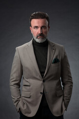Fototapeta premium Portrait of a stylish elegant senior businessman with a beard and casual business clothes in photo studio isolated on dark background gesturing with hands