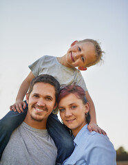Fototapeta premium Enjoying a family day outdoors. Portrait of smiling mother and father carrying there little boy on their shoulders outside.