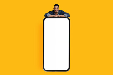 Handsome arab guy leaning on big smartphone with empty screen