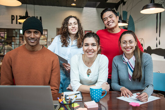 Smiling multiethnic coworkers looking at camera making team picture in multifunctional room of the pizza restaurant for working brunch - Diverse work group laugh posing for photo at workplace