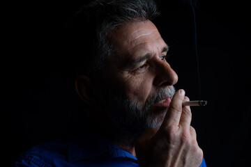 Man smoking cigarette on black background. Mystery man with cigar and smoke isolated on black background. Bearded man  smoking cigarette. Man smoking a cigarette. Cigarette smoke spread.