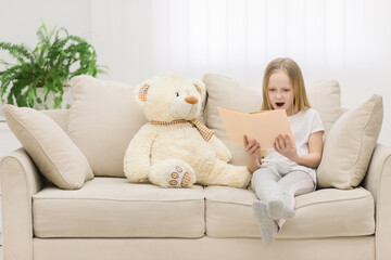 Photo of blond girl reading a book to her toy plush friend.
