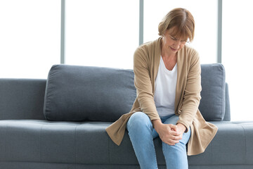 senior woman suffering from knee ache on sofa
