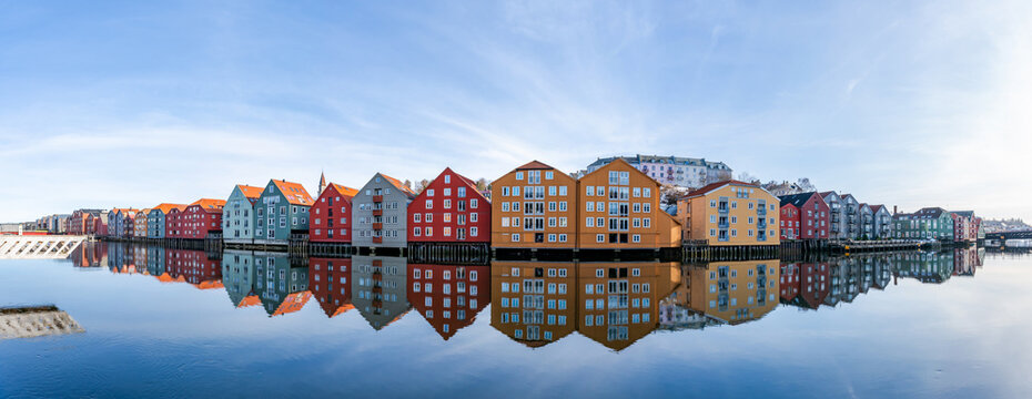 Wide panoramic view of old colorful wooden houses with reflections in river Nidelva in the Brygge district in Trondheim, Norway