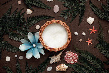 Wicker basket in fern leaves with shells and a flower on a brown background