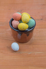 clay bowl with chocolate easter eggs wrapped in colored paper on wood