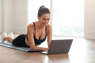 Young woman lying on yoga mat using laptop