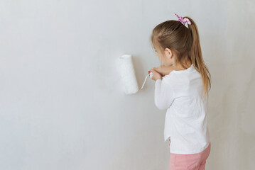 child girl 8 years old  paints the wall with white paint with a brush at home DIY repair
