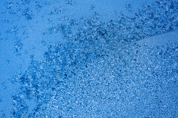 Fototapeta na wymiar Pattern or pattern of frost and snowflakes on frozen glass of window. Christmas back. Macrophotography. Flat empty snow-covered surface of blue color.