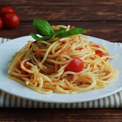 Spaghetti pasta with tomatoes and basil on a wooden table.
